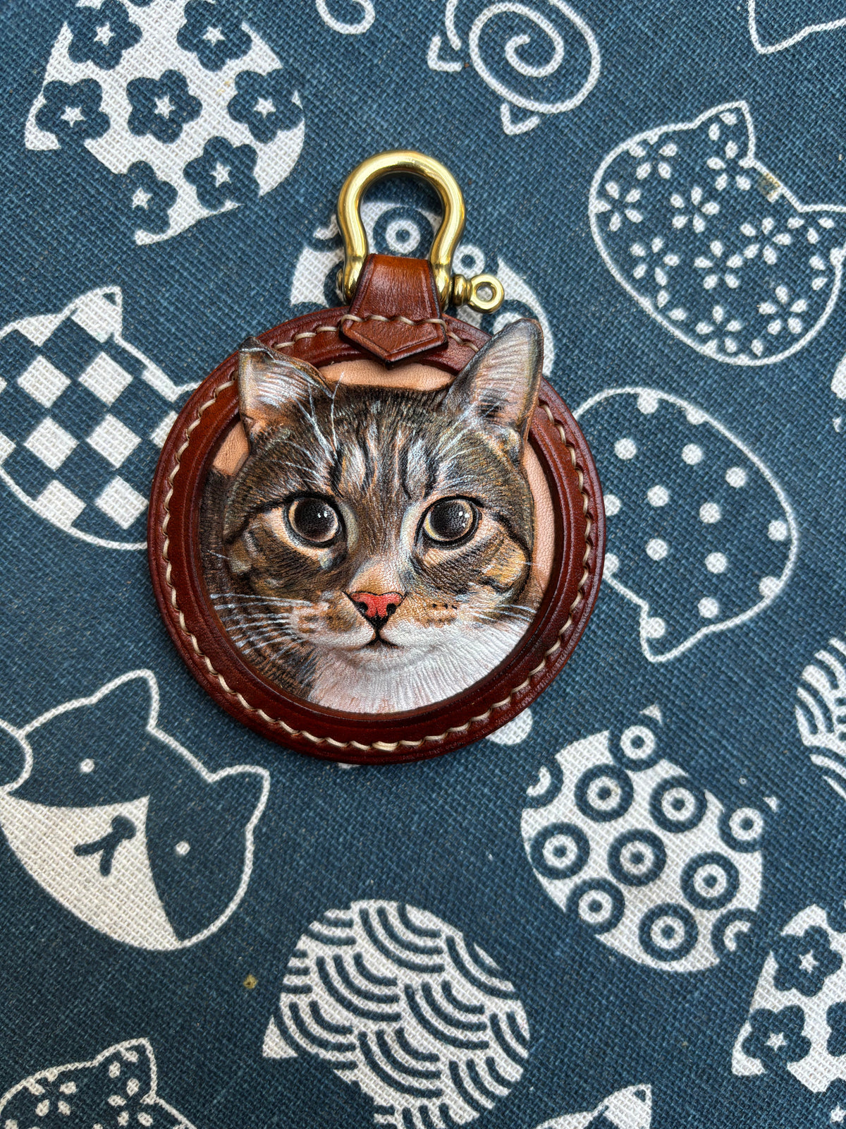 Hand-carved tabby cat leather keychain on patterned fabric